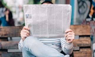 Eine Person sitzt auf einer Parkbank und hält sich lesend eine Zeitung vor das Gesicht. (Fotografie von Roman Kraft, www.unsplash.com)