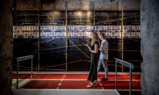 mann und frau laufen durch gang mit altersangaben und -infos sowie portraits an den wänden