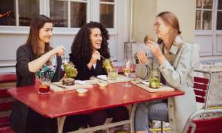 Drei junge Frauen sitzen an einem roten Tisch und essen Bagel und Salat.