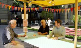 Drei Personen haben Platz genommen am Plaudertisch im Innenhof des Berner Generationenhaus und tauschen sich aus.