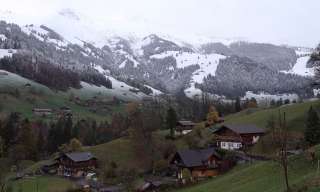 Blick auf ein Bergdorf, im Hintergrund sind verschneite Berge zu sehen.