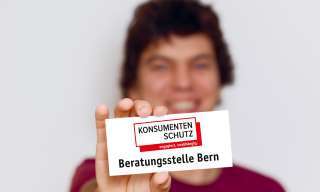 Eine Frau zeigt ein Schild, auf dem "Konsumentenberatung Bern" steht.
