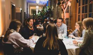In den Korridoren des Berner Generationenhaus sitzen an mehreren grossen Tischen Menschen, die zusammen essen und diskutieren. 