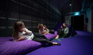 Der "Raum zum Scheitern" im Berner Generationenhaus. Drei junge Frauen liegen oder sitzen auf grossen violetten Kissen und hören sich via Kopfhörer Geschichten an.