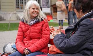 Zwei Dialoger:innen sitzen im Innenhof des Berner Generationenhaus auf einer Bank und unterhalten sich.