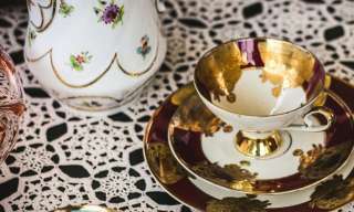 Porzellantassen und ein Krug auf einer gehäkelten Decke.