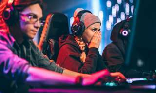 Drei junge Menschen sitzen vor Bildschirmen und gamen.