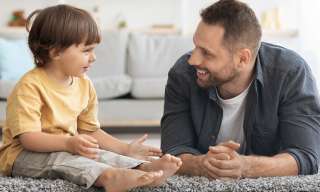Ein Mann liegt bäuchlings auf dem Boden und unterhält sich mit seinem Sohn.