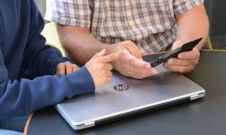 Ein jugendlicher Mensch erklärt einem älteren die Funktionen eines Handys.